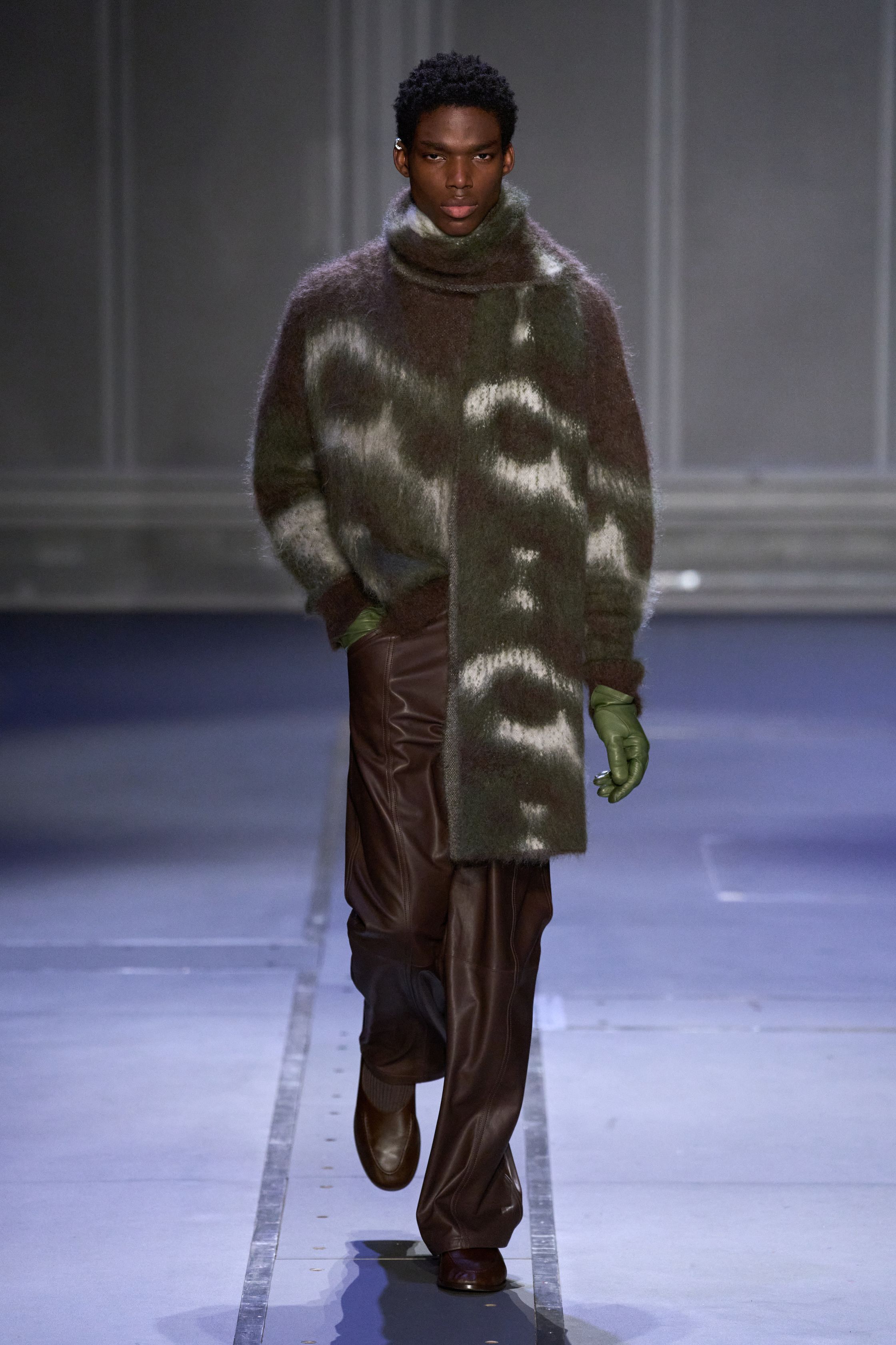 Études Studio 26FW 延续其标志性的“巴黎青年智识气质”，在克制的灰、棕、墨绿与深紫中，将街头轮廓与艺术语境并置。摄影肖像印花、皮革长风衣、渐变针织与蓬松羽绒共同构建出一种略带疏离感的城市诗意。系列并不追求强烈戏剧冲突，而是通过材质反差与比例控制，呈现介于学院派、亚文化与当代艺术之间的中间地带，体现 Études 一贯的文化策展式设计方法美-顽石频道趋势研究